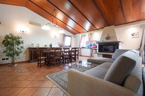 A cozy living room with a wooden ceiling, a sofa, a dining table with chairs, a TV, and a fireplace.