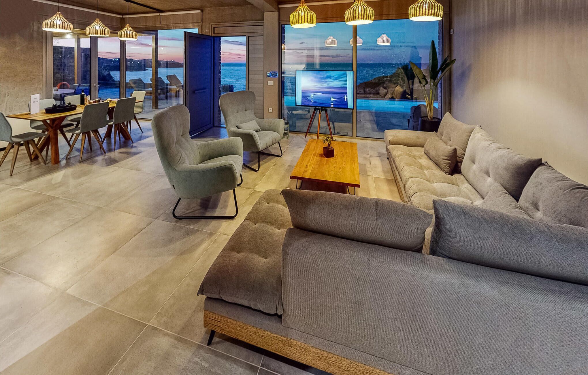A modern lounge area with a sofa, armchairs, a coffee table, and a TV screen displaying a scenic view.