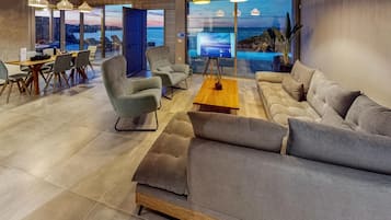 A modern lounge area with a sofa, armchairs, a coffee table, and a TV screen displaying a scenic view.