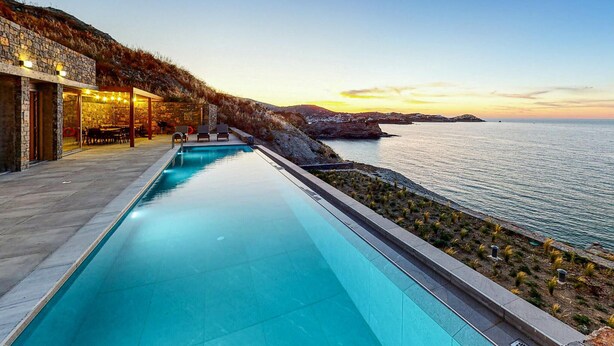 A swimming pool with a view of the sea and a building with outdoor seating.