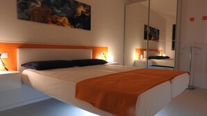 A modern bedroom with a large bed, a bedside table, a nightstand, a floor lamp, and a large mirror.