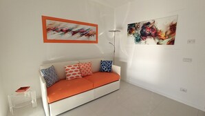 A modern living room with a white sofa, colorful cushions, and two abstract paintings on the wall.