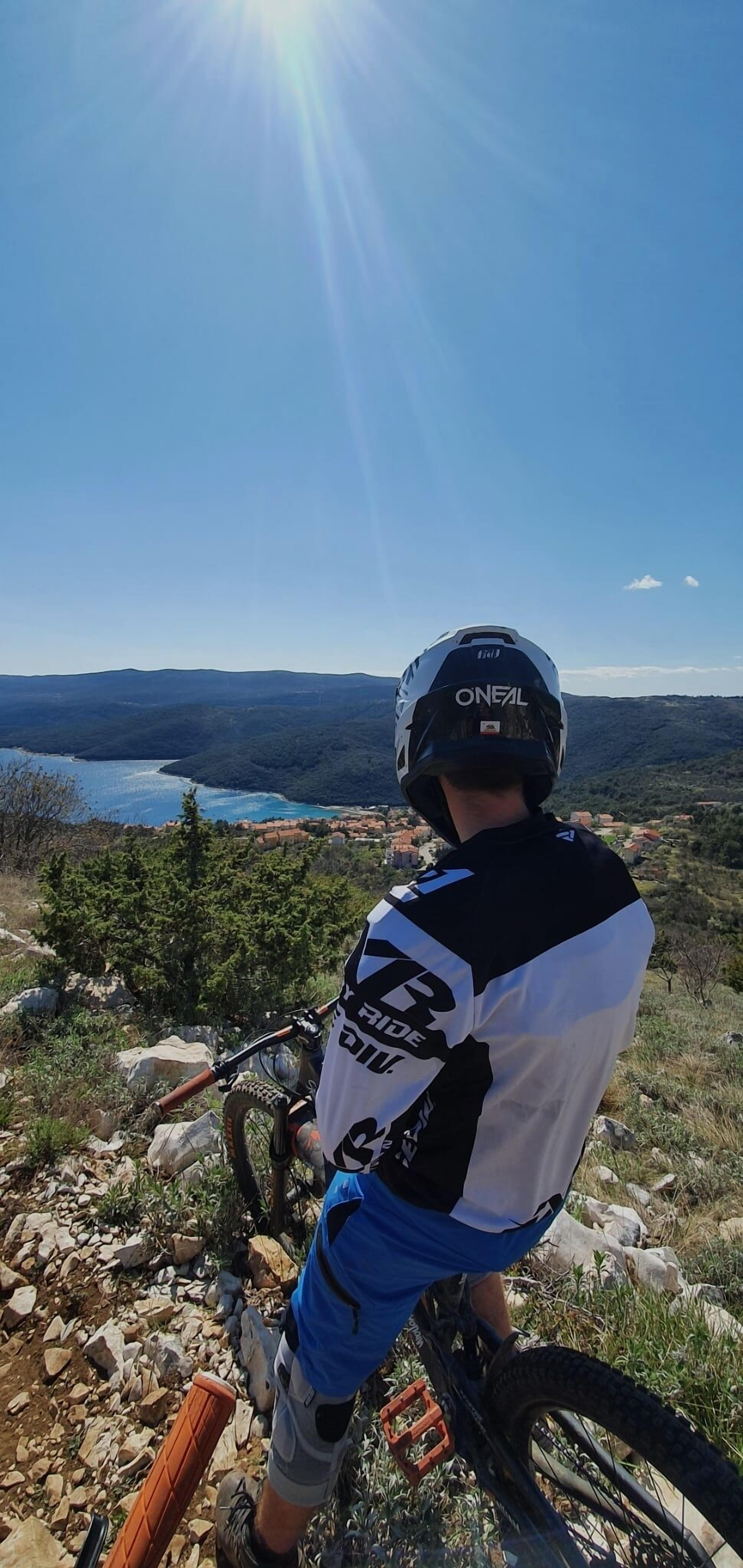 En person på en mountainbike med udsigt over et smukt landskab med en sø og bakker i det fjerne.