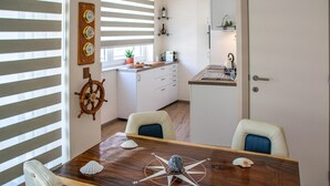 A dining area with a wooden table, chairs, a compass, and a ship's wheel on the wall. - Residentie Sint-Paulus (Oostende)
