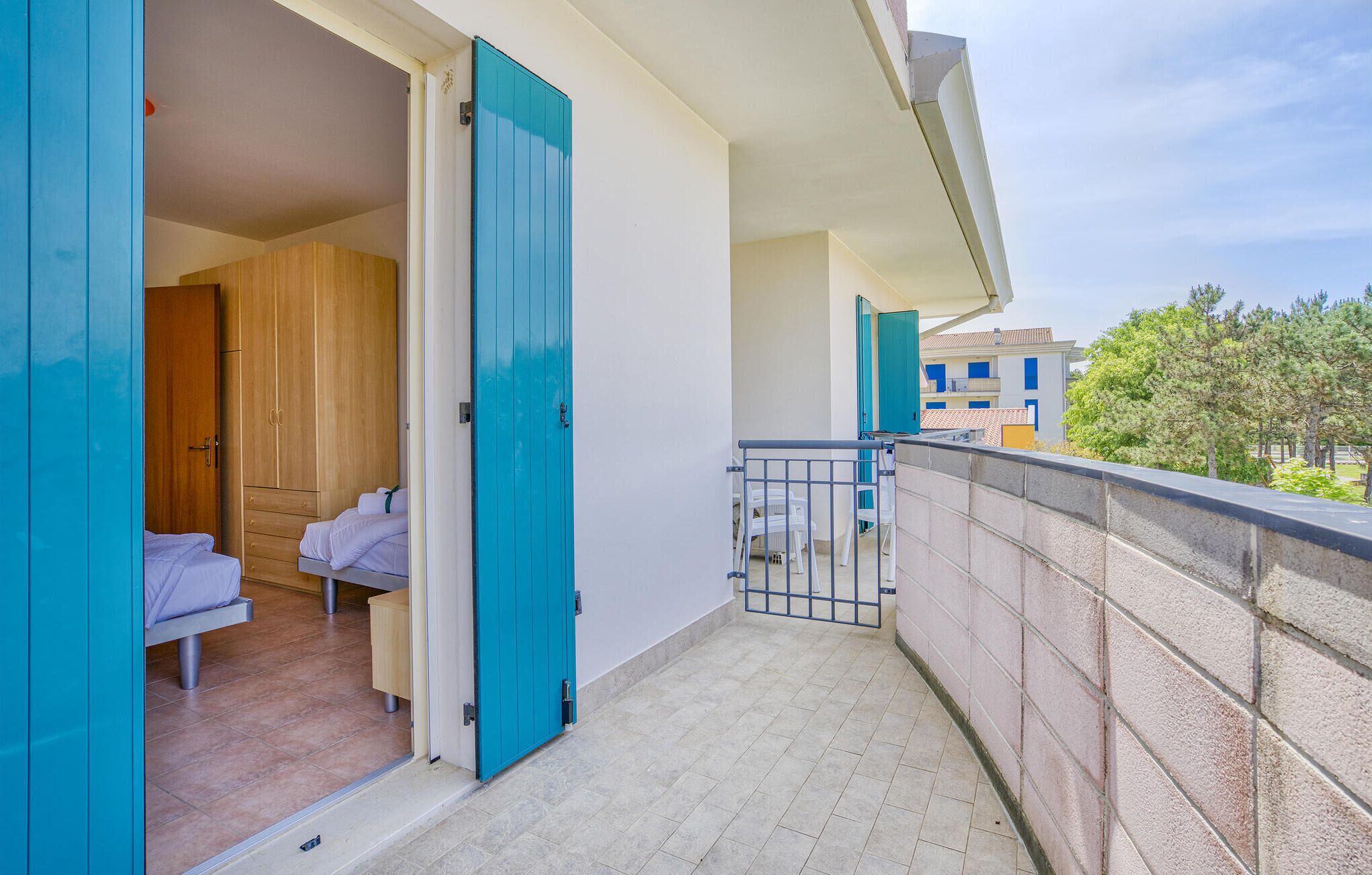 Un balcon donnant sur un quartier résidentiel, une porte en bois et un lit avec un matelas et des oreillers blancs.