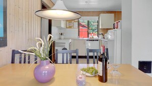 Un coin repas avec une table dressée pour deux personnes, agrémenté d’un vase violet contenant des plantes, d’une bouteille de vin et d’une assiette de raisins.