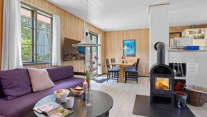 Un salon chaleureux avec un canapé violet, un coin repas avec une table et des chaises, une cheminée et un coin cuisine équipé de placards et d’un four à micro-ondes.