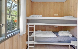 A bunk bed room with wooden walls, a window, and a small table.