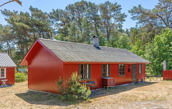 A red wooden cabin with a metal roof, a chimney, and a small patio area with outdoor seating.