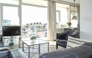 A modern living room with a large window, a flat-screen TV, a glass coffee table, and a leather sofa. - Nice apartment in Bergen aan Zee (Bergen aan Zee)