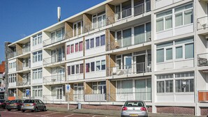 Un immeuble résidentiel à plusieurs étages, doté de balcons, d’un espace de stationnement et surplombant un ciel bleu dégagé.