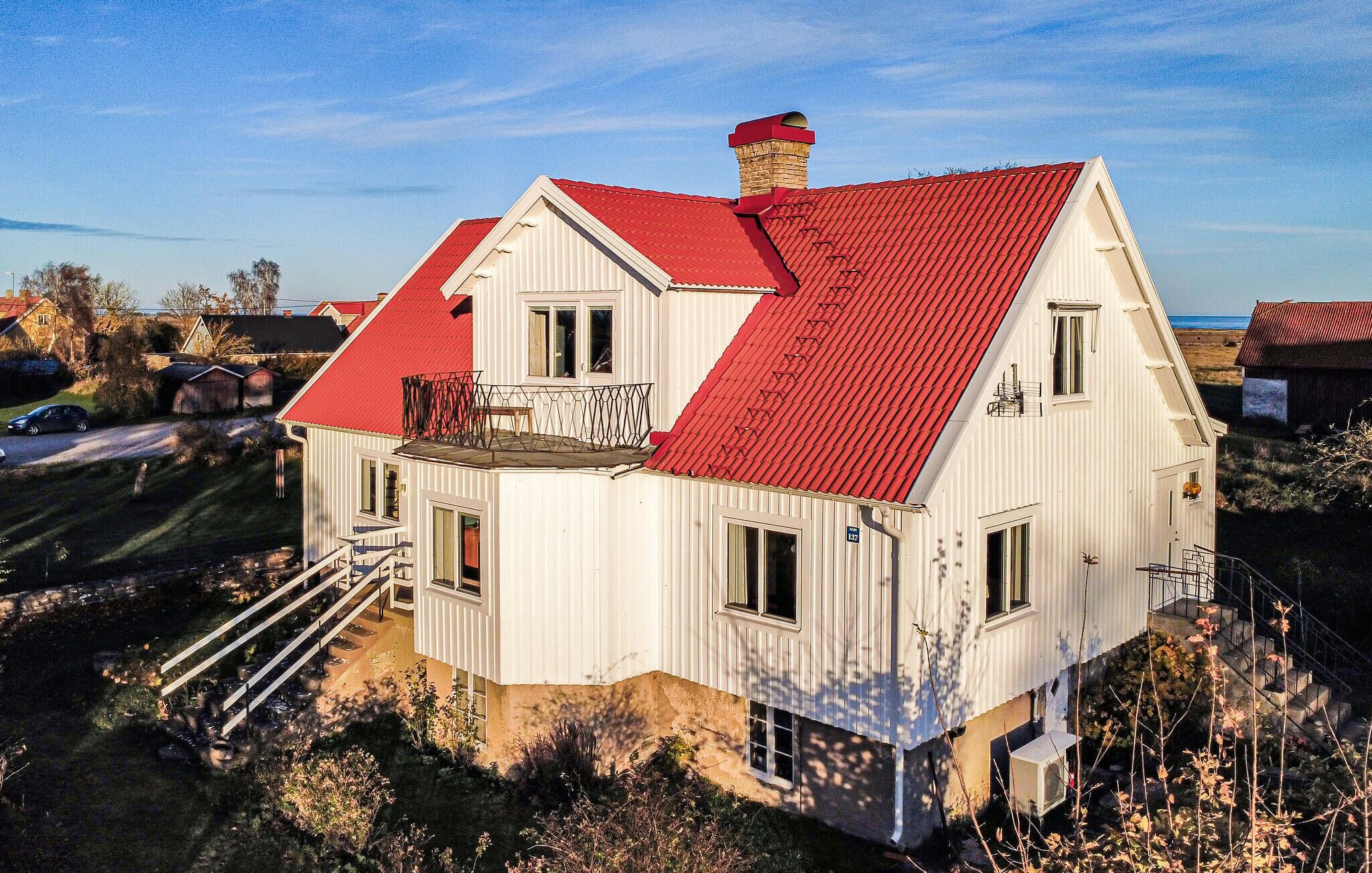 Une maison blanche à deux étages, avec un toit rouge, un balcon et un petit porche.