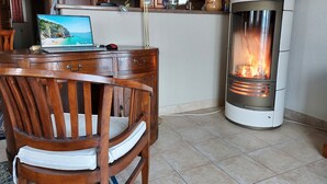 Una mesa de comedor de madera con sillas, una computadora portátil y un estufa de leña en una cocina.