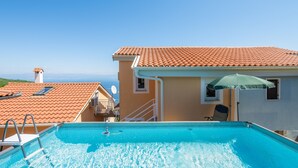 Una piscina con vista despejada al mar, techo de baldosas y una silla bajo una sombrilla.