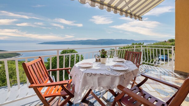 Una terraza con una mesa dispuesta para comer, con vistas panorámicas al mar y las montañas.