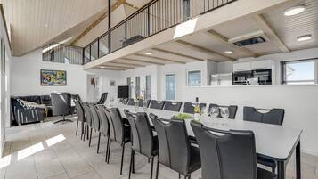 Ein geräumiger Essbereich mit einem langen Tisch und mehreren Stühlen, ein Küchenbereich mit modernen Geräten und ein Balkon mit Geländer.