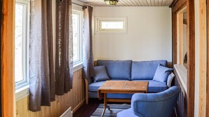 A room with a wooden interior, a blue sofa, a small wooden table, and a window with curtains. - Gorgeous home in Mollaryd with WiFi (Mollaryd)