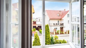 En vy genom ett fönster i en bostadsbyggnad med ett rött tegeltak, balkonger och en klar himmel.