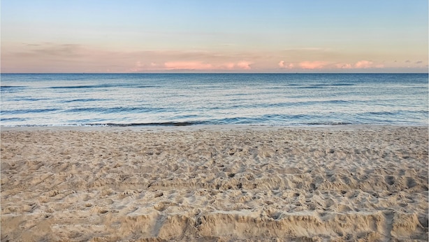 En strand med en sandstrand och havet i bakgrunden.