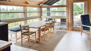 Een ruime kamer met een grote houten tafel en stoelen, grote ramen met uitzicht op de omgeving, en een gezellige zithoek met een blauwe stoel.