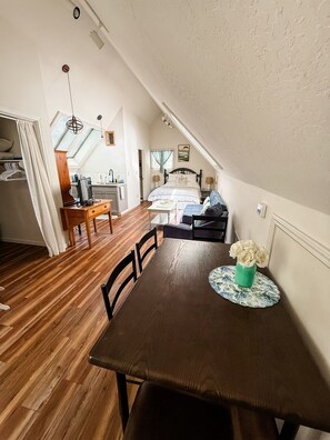 Un dormitorio acogedor en el ático, con techo inclinado, una mesa de comedor de madera y vistas a la cocina.