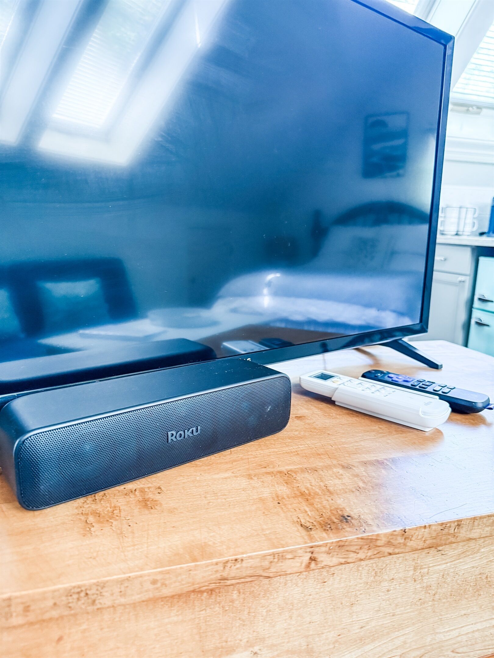 Televisor de pantalla plana, un dispositivo de transmisión Roku y dos controles remotos sobre una superficie de madera.