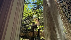 Une vue à travers une fenêtre, avec la lumière du soleil qui entre à flots, un poteau en bois et un rideau à motifs.