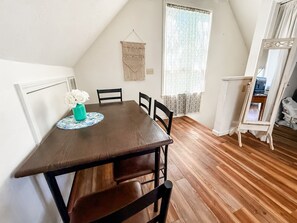 Un comedor con una mesa de madera, cuatro sillas, un jarrón con flores y un colgador de macramé en la pared.