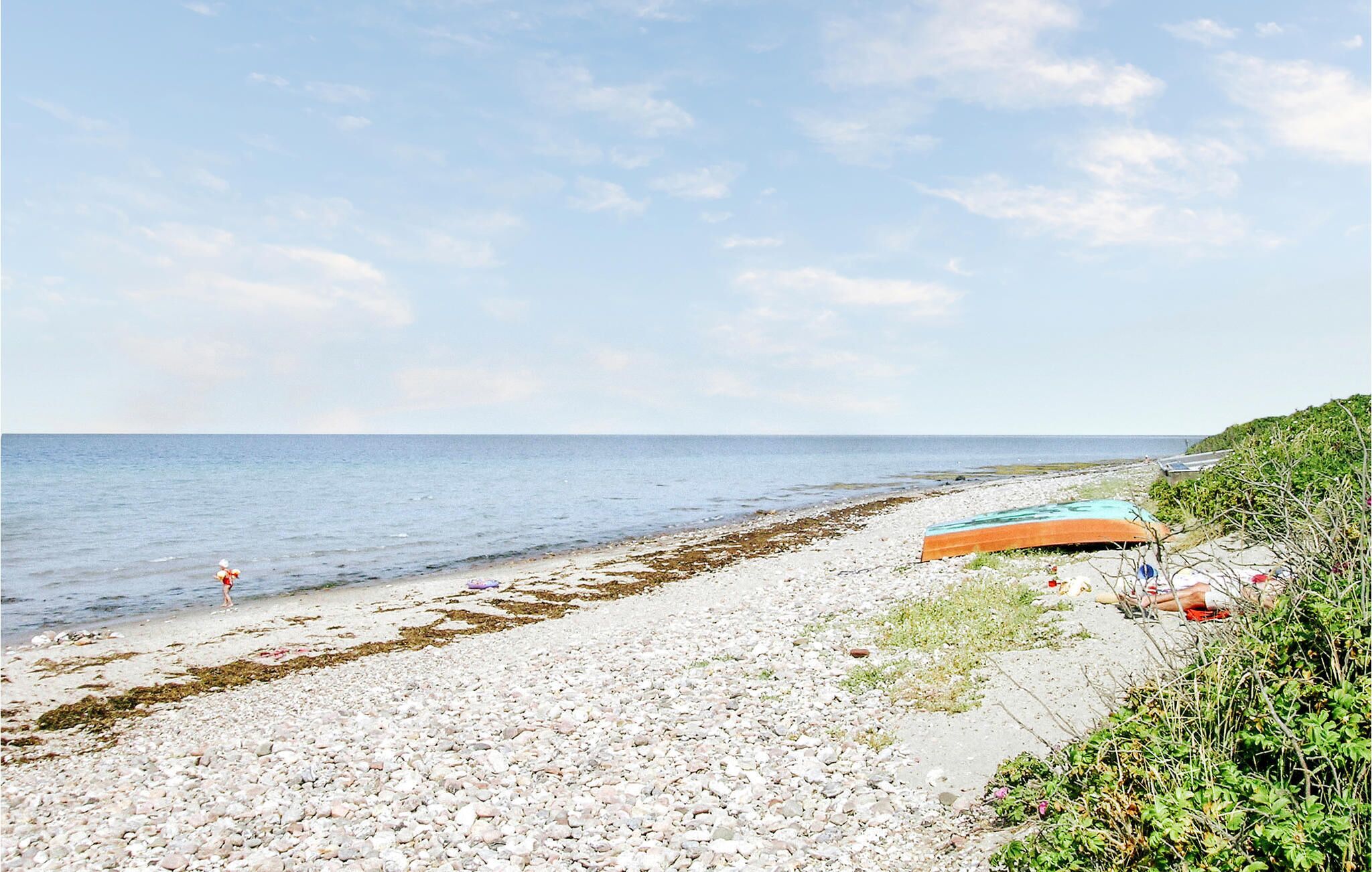 A pebbly beach with a clear sky, a few people, and a boat on the shore.
