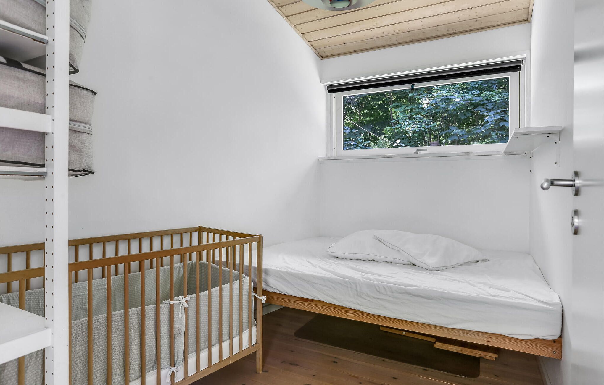 Een klein appartement met één kamer, voorzien van een houten ledikant, een bed met witte lakens, een raam met uitzicht op bomen en een witte muur.