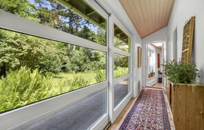 A hallway with large windows, a wooden ceiling, and a patterned rug.