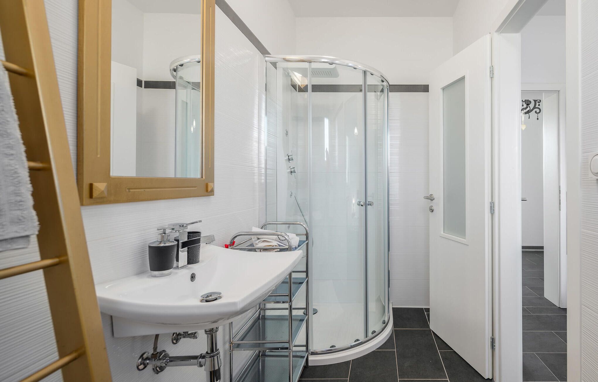Une salle de bain moderne avec une douche à parois de verre, un lavabo blanc avec un miroir et un porte-serviettes.