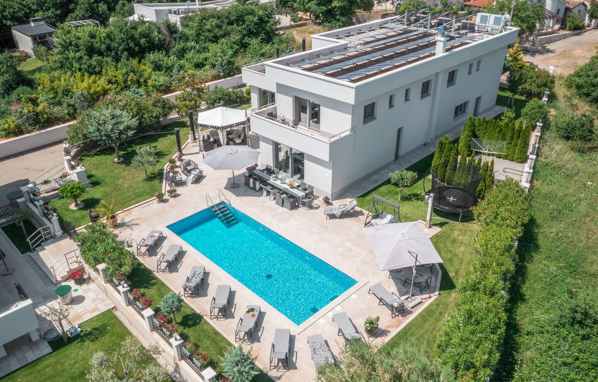 En modern byggnad i två våningar med en takterrass, en swimmingpool och utomhusområden med sittplatser.