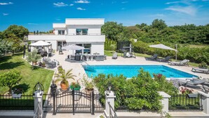 Ein modernes, zweistöckiges Haus mit Swimmingpool, Gartenmöbeln und üppiger Bepflanzung.