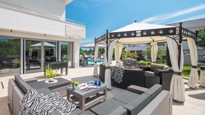 Eine Terrasse im Freien mit Korbmöbeln, einem Glastisch und einem überdachten Sitzbereich.
