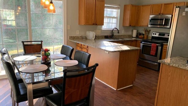 Una cucina moderna con mobili in legno, un'isola centrale, elettrodomestici in acciaio inossidabile e un'area pranzo con tavoli e sedie in vetro.