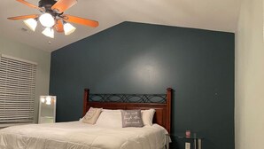 Una camera da letto con un letto, una ventola a soffitto, un comodino e una parete di colore scuro.
