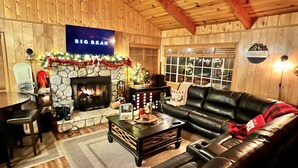 A cozy living room with a stone fireplace, a black leather sofa, and a coffee table. - Cozy Cabin • Near Zoo, Golf, Trails, Lake • Family & Dog Friendly • Game Room (Big Bear Lake)