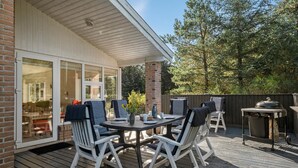 Een terras buiten met een tafel, stoelen, een barbecue en uitzicht op een gebouw met bakstenen en glazen deuren.