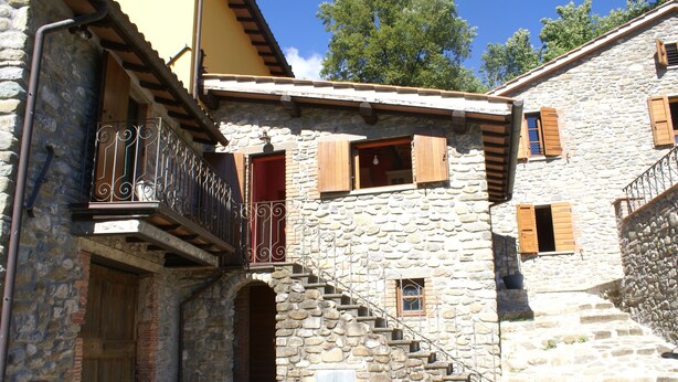 A stone building with a wooden door, a balcony with wrought iron railings, and a staircase leading to an upper level. - Tuscan tradition renovated in 2021 (Barga)