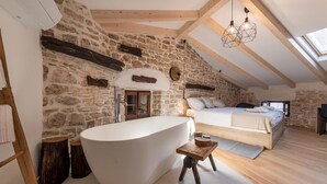 Camera da letto con parete in pietra, vasca da bagno ampia, soffitto in legno e finestra a lucernario.