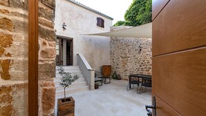 Un edificio in pietra con una scala che porta a una porta, un tavolino con sedie e un baule di legno.