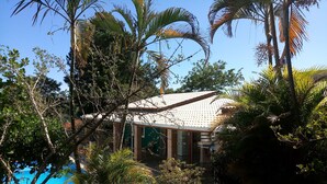 Une maison avec un toit en tuiles, entourée d’une végétation luxuriante et dotée d’une piscine.