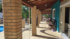 Un patio couvert avec des piliers en briques, une piscine et du mobilier d’extérieur.