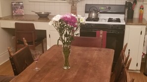 Una mesa de madera con sillas, un florero con flores y una cocina al fondo.