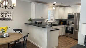 A modern kitchen with white cabinetry, a central island, a dining area with a round table and chairs, and a chandelier. - Redding Country Cottage (Redding)