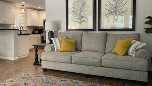 A living room with a grey sofa, two yellow cushions, a patterned rug, and framed botanical artwork on the wall. - Redding Country Cottage (Redding)