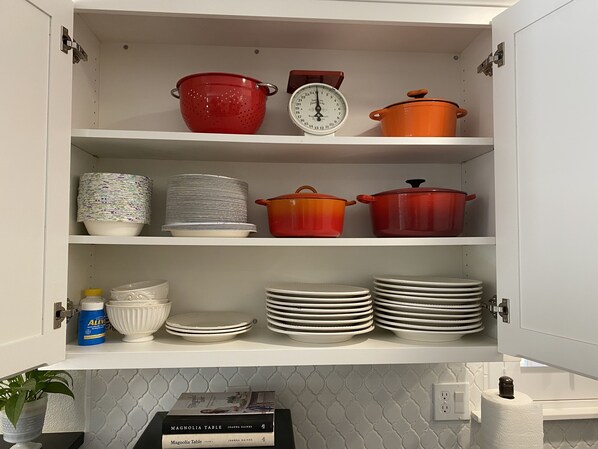 A kitchen cabinet with shelves containing various kitchenware, including pots, pans, and plates. - Redding Country Cottage (Redding)