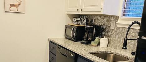 A compact kitchen with white cabinets, a microwave, a coffee maker, and a sink.
