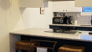 A compact kitchen with a granite countertop, a coffee maker, and a microwave. There is a dining area with a glass table and woven chairs. - Cozy Cabin with fireplace and screened in porch in Sapphire Valley. (Sapphire)